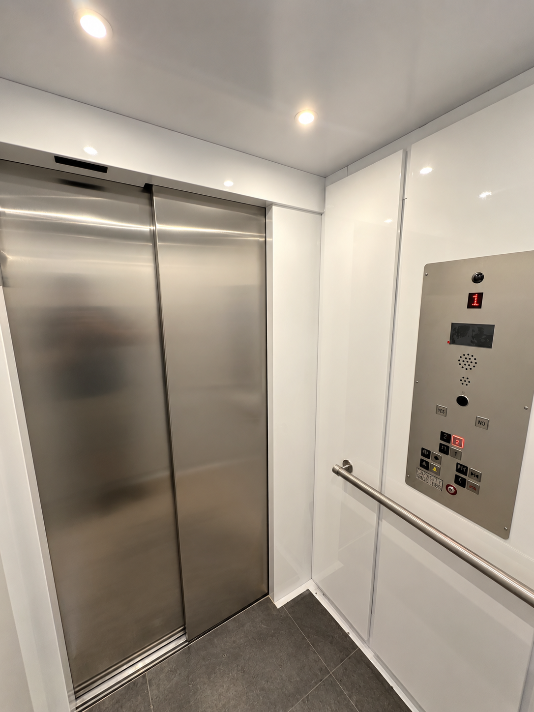 Inside a LU/LA elevator cab with white panels, handrail, tile floor, and ADA control panel